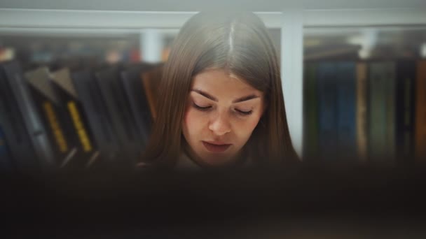 Mujer detrás de las estanterías leyendo libro interesante — Vídeos de Stock