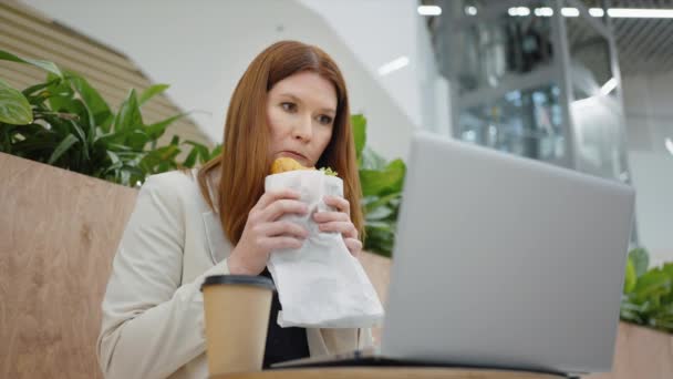 サンドイッチを食べてノートパソコンでビデオを見ているビジネスマンの女性 — ストック動画