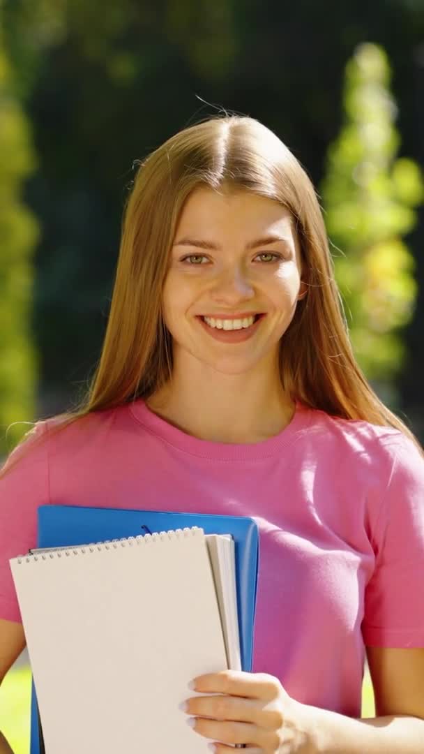 Vertical Screen: Female student with books in hands standing in park — Stockvideo