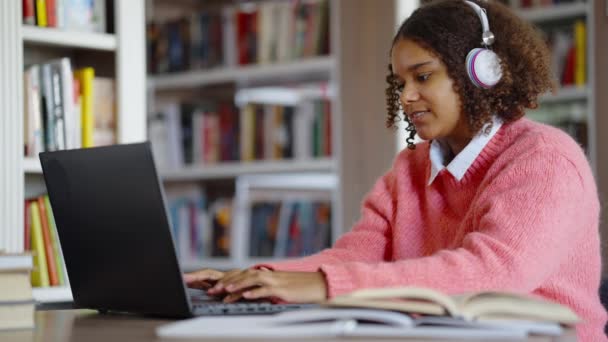 Afro-Amerikaanse student werkt aan laptop in bibliotheek — Stockvideo