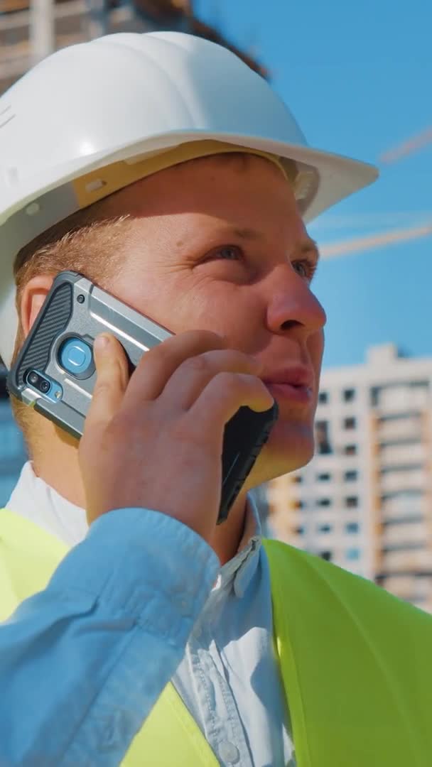 Vertical Screen: Civil engineer talking on phone against construction site — Stock Video