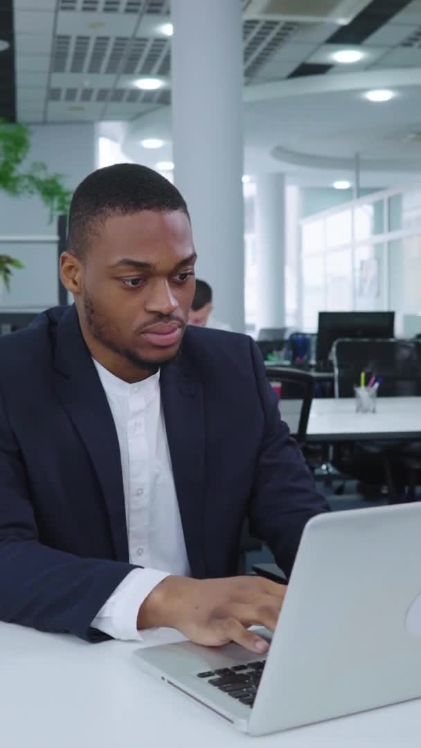 Vertical Screen: Black businessman working on laptop in open space office — Stockvideo