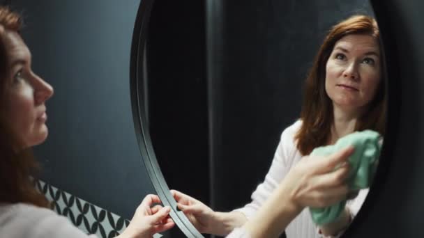 Усміхнена жінка прибирає дзеркало у ванній — стокове відео