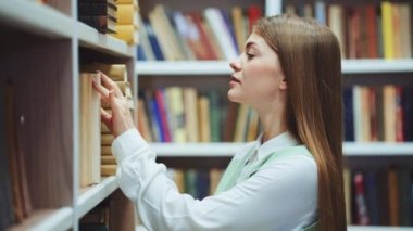 Kütüphanedeki kitaplıktan kitap seçen kadın