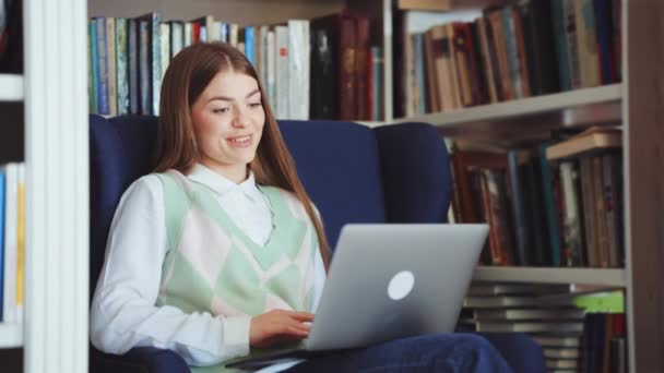 Vrouw chatten online via laptop in de bibliotheek — Stockvideo