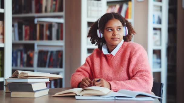 Chica negra estudiante escuchando música en la biblioteca — Vídeo de stock