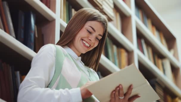 Vrouw die grappig boek leest in de bibliotheek — Stockvideo