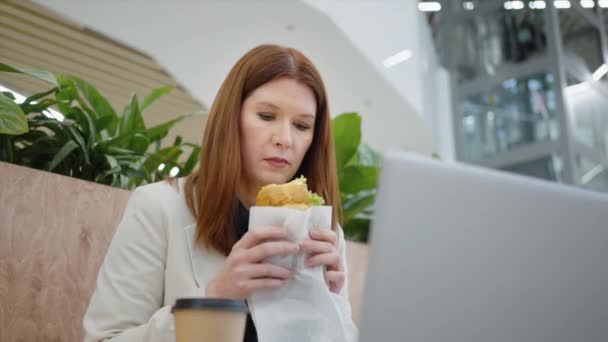 Empresária na pausa para almoço comer sanduíche e assistir vídeo no laptop — Vídeo de Stock