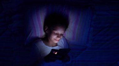 Çocuk gece yatakta akıllı telefonda oynuyor.