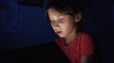 Karanlıkta tablet kullanan küçük kız.
