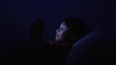 Kız gece yatakta yatarken akıllı telefondan program izliyor.