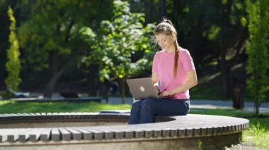 Öğrenci parkta dizüstü bilgisayar kullanarak çalışıyor