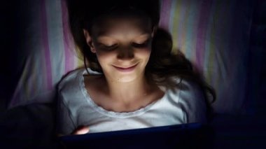 Yatakta yatan ve tablette video izleyen bir kız.