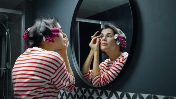 Женщина наносит макияж, глядя в зеркало — стоковое видео