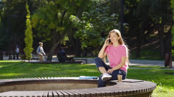 Жінка сидить у парку і розмовляє по телефону — стокове відео