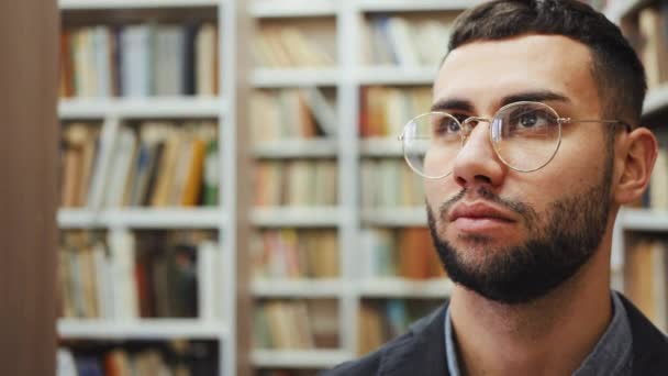 Uomo con gli occhiali che cammina in biblioteca e cerca libri — Video Stock