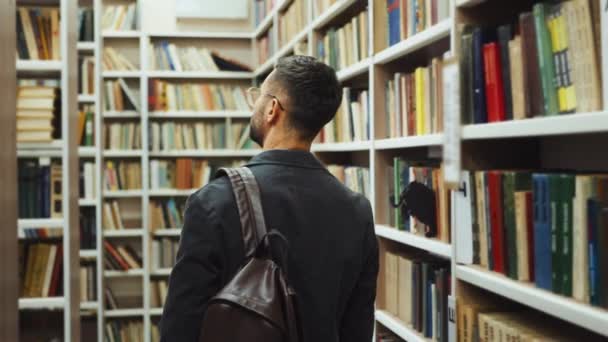 Estudante caminhando na biblioteca entre estantes — Vídeo de Stock