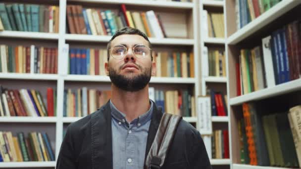 Студент смотрит на книжные полки в библиотеке — стоковое видео