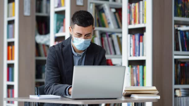 Student studiujący w bibliotece przy użyciu laptopa podczas pandemii — Wideo stockowe