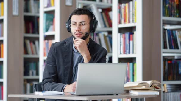 Homem de óculos usando headset para ensino à distância na biblioteca — Vídeo de Stock