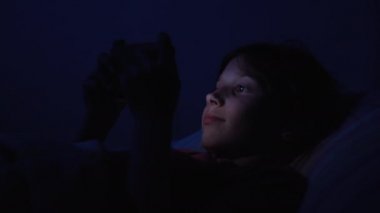 Çocuk yatakta aletle eğleniyor.