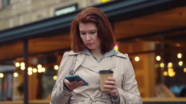 Ενηλίκων θηλυκό πίνοντας καφέ και χρησιμοποιώντας το τηλέφωνο στο δρόμο — Αρχείο Βίντεο