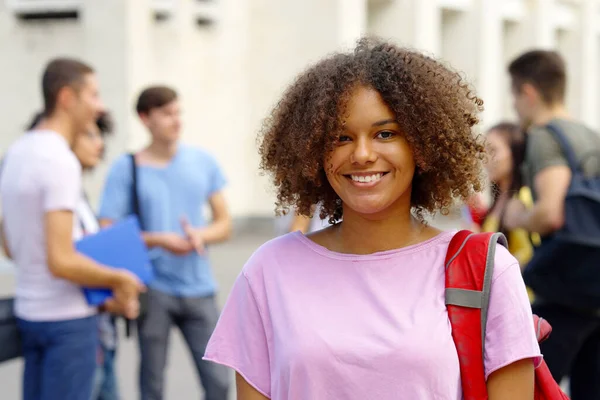 Üniversite binasının yakınındaki kameraya gülümseyen siyah kız öğrenci.