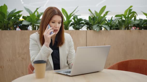 Mujer de negocios hablando por teléfono y utilizando el ordenador portátil — Vídeo de stock