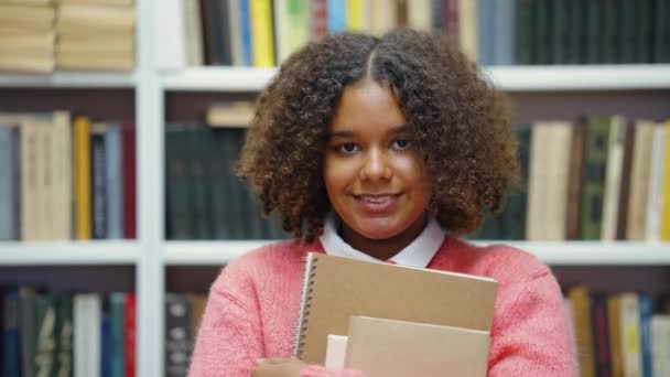 Verlegen meisje knuffelen boeken in college bibliotheek — Stockvideo