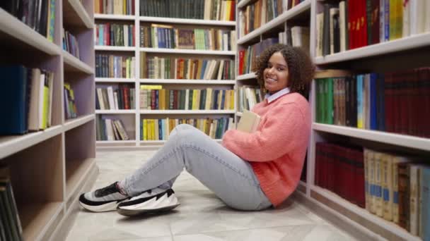 Μαύρη φοιτήτρια κάθεται στο πάτωμα της βιβλιοθήκης — Αρχείο Βίντεο