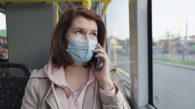 Maskeli kadın otobüse binerken telefonla konuşuyor.
