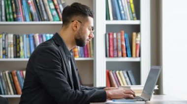 Kütüphanede araştırma için dizüstü bilgisayar kullanan adam