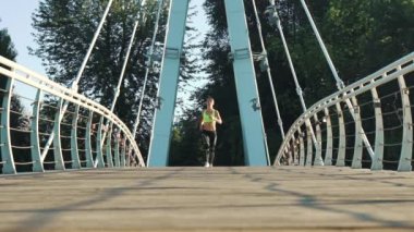 Ağır çekim kadın sabah güneşinde köprüde koşuyor.