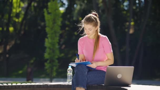 Frau macht sich Notizen im Park und benutzt Laptop — Stockvideo
