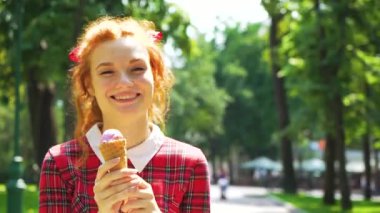 Gülümseyen kızıl saçlı kız güneşli bir günde parkta dondurmayla yürüyor.