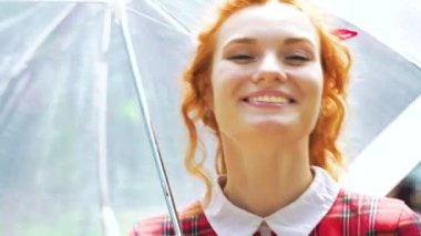 Kızıl saçlı, çilli kadın elinde şemsiyeyle kameraya gülümsüyor.