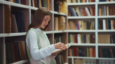 Female reader standing by bookcase and reading book