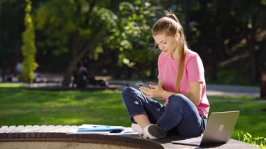 Parkta akıllı telefondan mesaj atan mutlu kız öğrenci.