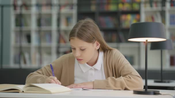Chica Escuela Ropa Casual Sentado Mesa Escritura Libro Ejercicios Estanterías — Vídeos de Stock