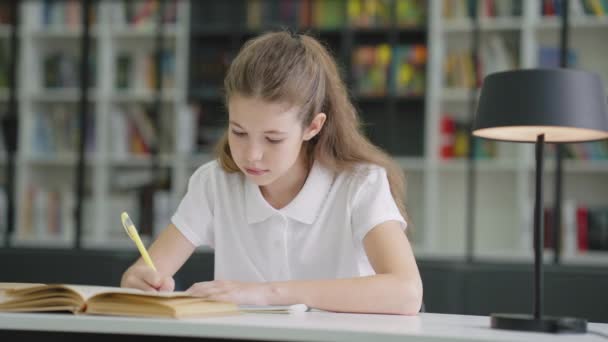 Niña Escuela Vistiendo Una Camiseta Blanca Sentada Mesa Escribiendo Libro — Vídeo de stock