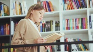 Akıllı çocuk kitap raflarının yanında durup kitap okuyor. Düşük açılı yay, sıradan giyinen liseli kızı kitapçıda ya da kütüphanede edebiyatın keyfini çıkarırken çekti. Eğitim kavramı