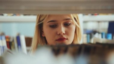 Kitap raflarında kitap arayan sarı saçlı genç bir kadının yakın plan portresi. Kütüphanede fotoğraf çeken öğrenci, kitapçıda en sevdiği baskıyı arayan okuyucu. Eğitim kavramı