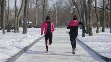 Kış parkında dar yolda koşan pembe ve siyah giysili kadın ve erkek. Açık hava aktivitelerinden hoşlanan bir çifti takip ediyoruz. Sağlıklı bir yaşam tarzı. Spor anlayışı