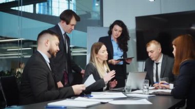 Business people gathering together in office, having meeting, discussing projects, working with papers, laptop, one woman using tablet. Planning strategy, communication of executives