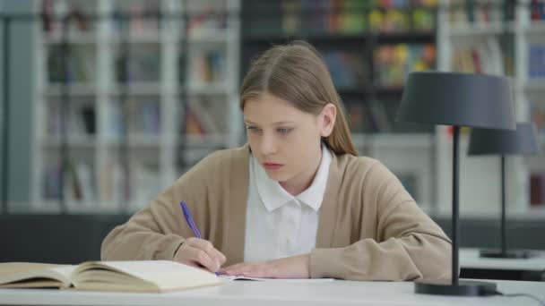 Smart Girl Casual Wear Sitting Desk Writing Exercise Book Bookshelves — Vídeo de Stock