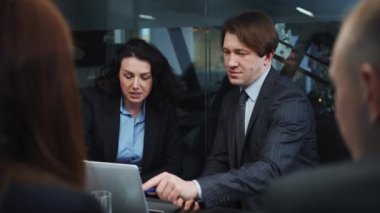 Business people in official wear sitting in office, looking at laptop and discussing latest information, viewed over shoulders of other colleagues. Online business. Concept of technology