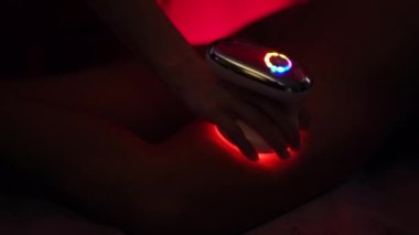 Hands of therapist massaging female hip with anti-cellulite equipment emitting red light. Partial view of spa customer getting skin care treatment. Concept of wellness