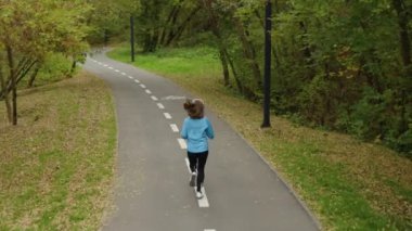 Female jogger in sports wear running in slow motion in park in the morning, autumn leaves lying on ground, following shot from above. Healthy lifestyle and outdoor activity