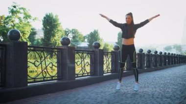 Active woman exercising and jumping in city park. Attractive fit girl training warming up at morning outdoors. Healthy, fitness, wellness lifestyle. Sport, cardio, workout concept