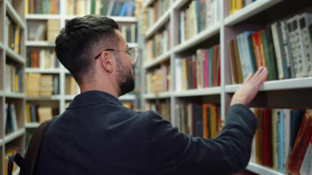 Männlicher Student Mit Brille Und Jacke Spaziert Bücherregalen Vorbei Auf — Stockvideo
